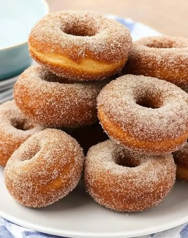 Freshly fried gluten-free yeast donuts being dusted with powdered sugar
